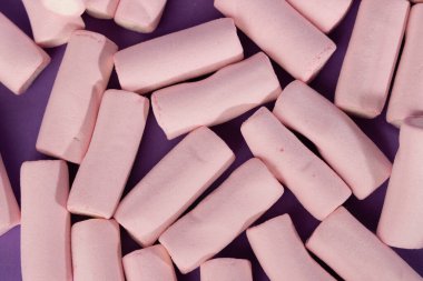 Dağınık şekerlemelerin detaylı üst görüntüsü, yatay fotoğrafın sol tarafında yer alıyor. Şekerlemeler, koyu mor bir arkaplan karşısında neşeli, renkli bir sahne oluşturur.