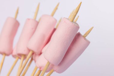 Horizontal image showing skewers with marshmallows, placed on the left side of a white backdrop. The marshmallows are in perfect alignment for toasting clipart