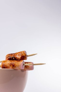 Beyaz arka planda pembe bir kasede mükemmel bir şekilde kızartılmış marshmallow şişlerinin ayrıntılı dikey görüntüsü. Şişler solda, kaseyle lokum arasındaki kontrastı vurguluyor..