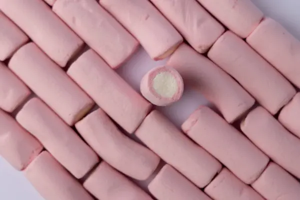 stock image Top view of neatly arranged marshmallows with one lifted in the center of the row, creating a focal point. The vertical photo is set against a clean, white background, emphasizing the contrast