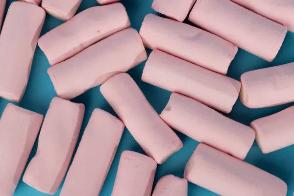 stock image A detailed top-down view of a disordered group of marshmallows filling the image. They are arranged haphazardly in the center of the horizontal shot, set against a vibrant blue background.