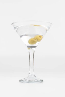 Görüntünün sol tarafına yerleştirilmiş iki zeytinli klasik bir martini bardağının yakın çekimi. Beyaz arka planda yer alan fotoğraf, kokteylin basitliğini ve zarafetini vurguluyor.