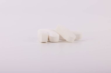 Tarafsız beyaz bir yüzeye sergilenen beyaz hapların odaklanmış görüntüsü, temiz, hassas tıbbi tedavi ve sağlık hizmetlerini vurguluyor