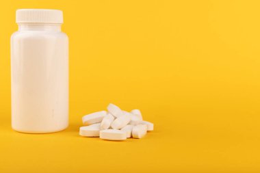 Altüst olmuş beyaz bir ilaç şişesinin yakın plan görüntüsü ve sarı arka plan üzerine yayılmış haplar. Tıbbi görüntüler için uygun