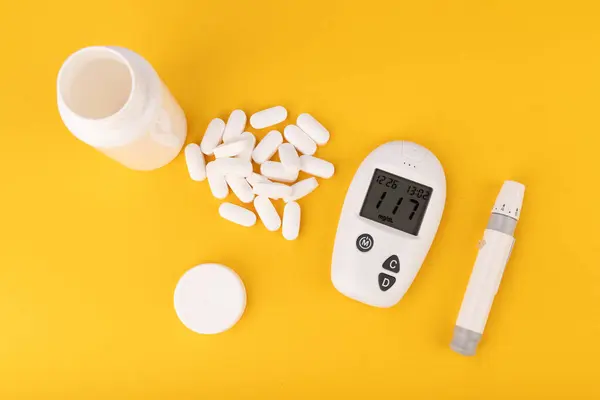 stock image Close-up of a glucose meter, white pills, and a hand taking a pill against a yellow background. Perfect for illustrating diabetes care and medication