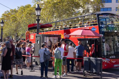 Barselona, İspanya - 15 Eylül 2024: Açık mavi gökyüzü altında canlı çift katlı turist otobüslerine binmek için Plaza Cataluna 'da bir turist kalabalığı sıraya dizildi