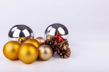 Çam kozalakları parlak kırmızı çanlar ve farklı boyutlarda altın-gümüş Noel süslemeleri ile güzelce dekore edilmiş, temiz beyaz arka planda kurulmuş.