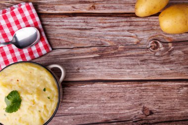 Tahta bir masada patates, kaşık ve kırmızı peçeteyle bir kase kremalı patates püresi. Şükran Günü titreşimleri kırsal ve rahatlatıcı bir dokunuşla