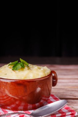 Kırmızı kareli peçete ve kaşığın yanında, kırsal ahşap bir masanın üzerinde duran kaymak gibi patates püresinin yakın çekim görüntüsü.