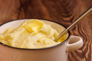 Eriyen tereyağlı inci ve kaşıkla kaymaklı patates püresi. Zarif bir şekilde zengin, koyu ahşap bir masanın üzerine yerleştirilmiş.