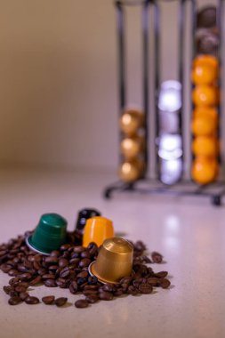 Kahve çekirdeklerinin üzerinde renkli kahve kapsüllerinin detaylı bir görüntüsü. Bir kapsül organizatörü arka planda zengin bir kahve sahnesinin altını çizerek bir yapı sağlar