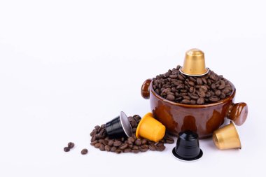 Kahverengi kahve fincanı üzerinde kapsül olan, dağınık fasulye ve renkli kapsüllerle çevrili, beyaz arka planda.