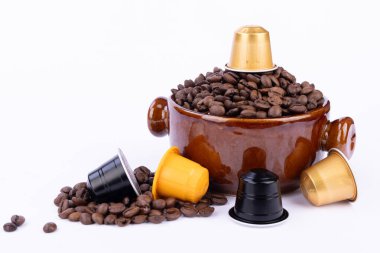 Kahverengi kâse kahve çekirdeği dolu, kapsülle kaplanmış, dağınık fasulyeler ve beyaz arka planda renkli kapsüller var.