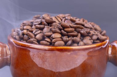 A brown bowl brimming with warm, freshly roasted coffee beans emits a rich aroma, perfectly contrasting with the elegant black background clipart