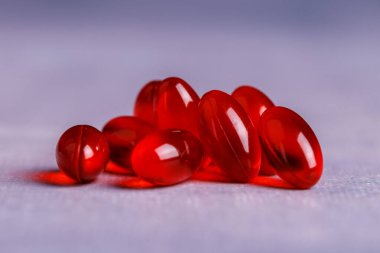 Beton bir masanın üzerindeki kırmızı şeffaf kapsüllerin yakın plan görüntüsü, parlak ve canlı renklerine odaklanarak, davetkar bir görsel yaratıyor