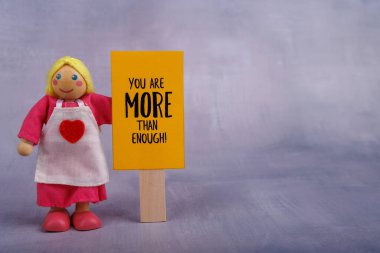 Tahta bir bebeğin elinde motive edici bir ifade gösteren turuncu bir tabela var. Basit ama güçlü mesaj pozitifliği ve ilhamı teşvik eder.