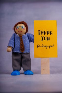 Tahta oyuncakçı, motivasyon sözleriyle sarı bir tabela tutar. Basit, minimalist bir şekilde pozitiflik ve umut yayar.