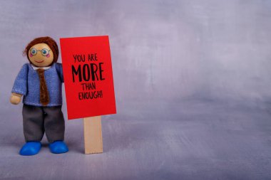 Tahta oyuncakçı gururla kırmızı bir tabela sergiler. Motivasyonal bir alıntı içerir. Gören herkese neşe ve pozitif enerji yayar.