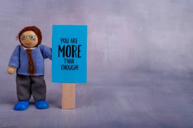 Tahta bir oyuncak heykeli mavi bir motivasyon işareti sergiliyor, pozitif ve ilham verici, canlı ve neşeli bir arka plana karşı dizilmiş