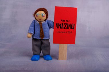 A whimsical wooden toy figure showcases a red motivational sign, promoting positivity and joy, perfect for brightening up any space clipart