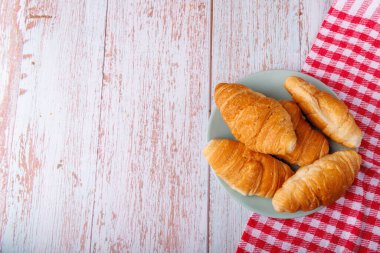 Buttery croissants rest on a light wooden table, viewed from above. The simple setting highlights the golden texture of the pastries against the natural wood clipart