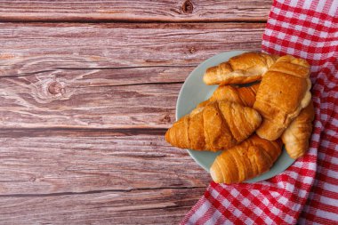 A top-down shot of golden croissants placed on a light wooden table. The photo captures their flaky texture and rustic presentation on the natural surface clipart