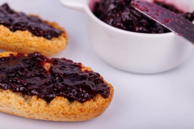 Beyaz arka planda bir kavanozun yanına yaban mersini reçeli serpiştirilmiş tost. Detaylı manzara bu kahvaltı sahnesine renk katar