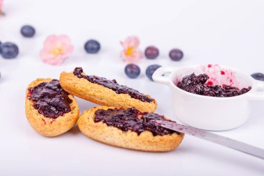 Yaban mersini reçelli tost ve beyaz arka planda bir kavanoz reçel, zengin rengi ve dokuyu vurguluyor.