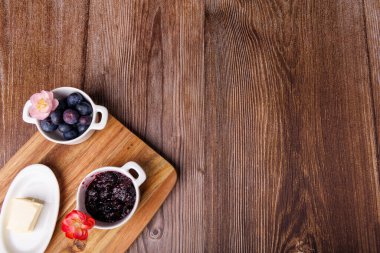 Kır kahvaltısının en üst görüntüsü. Koyu ahşap bir masada, tereyağı tabağının yanında, ekmek kızartma ve yaban mersini reçeli.