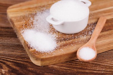 Yanında şeker dolu seramik bir kâse ve ahşap bir kaşık olan tahta bir masa. Yukarıdan çekilen, şekerin ve masanın dokusunu gözler önüne seren