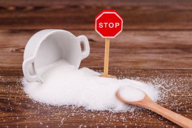 Bir seramik şeker kavanozu devrildi, tahtadan bir masaya şeker döküldü. Tahta bir dur levhası ve şeker dolu bir kaşık yakınlara konur ve kırsal bir manzara yaratır.