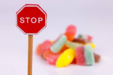 A wooden stop sign stands in front of a mountain of colorful gummy candies on a white background, creating a fun and eye-catching scene clipart