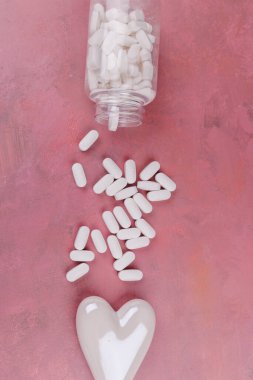 A romantic top-down shot with red and white porcelain hearts and white pills on a red cement table, symbolizing heart disease for Valentine's Day clipart