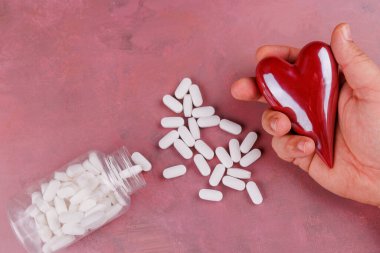 Sevgililer Günü 'nde kırmızı çimento yüzeyinde porselen kalpler ve beyaz hapların yer aldığı, kalp hastalıklarını sembolize eden bir fotoğraf çekilmiştir.