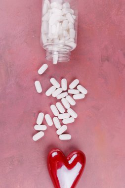 A red and white porcelain heart arrangement on a red cement table with white pills, symbolizing heart health, captured from a Valentine's view clipart