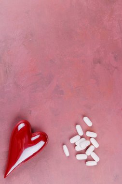 A top-down view of porcelain hearts and white pills on a red cement table, symbolizing heart health and love, capturing a Valentine's Day theme clipart