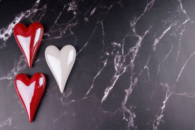 Siyah mermer bir yüzeye yerleştirilmiş canlı kırmızı ve beyaz porselen kalpler, Sevgililer Günü için aşk ve romantizm sergiliyor.