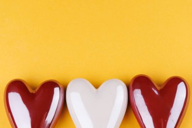 Sevgililer Günü kalpleri kırmızı ve beyaz porselenlerle sıralanmış sarı arka planda, yukarıdan görülüyor, aşkı ve kutlamayı simgeliyor.