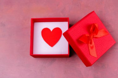 Lezzetli kırmızı bir hediye kutusu. Yay ile bağlanmış. Yürekten kırmızı bir kağıt kalp gösteriyor.