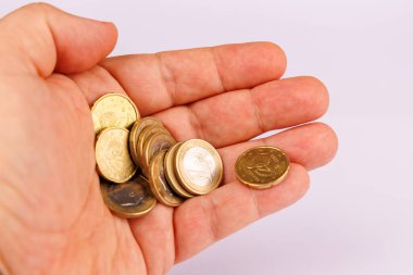 Avucunun içinde, finans, tasarruf veya zenginliği temsil eden beyaz bir arka plana yerleştirilmiş birkaç avro sikkeyi tutan bir elin yakın plan görüntüsü