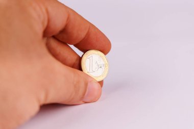 Parmakların arasında bir avroluk bir para, ekonomik ve parasal temaları vurgulayarak beyaz bir zemin karşısında özenle tutuldu