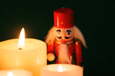 Orijinal saçlı büyüleyici bir fındıkkıran yanan mumların ve renkli Noel süslerinin yanında duruyor ve yeşil üzerine sıcak bir atmosfer yaratıyor.