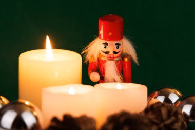 Orijinal saçlı zarif bir fındıkkıran, tatil için zengin yeşil arka planda mumlar ve şenlikli süslemelerle çevrilidir.