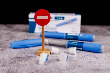 Diyabet tedavisi için kullanılan semaglutid enjeksiyon kalemlerinin yanına yerleştirilmiş tahta giriş işareti, çimento masa arkasında sergileniyor.