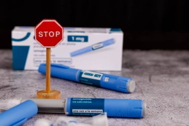 Diyabet yönetimi için semaglutit kalemlerinin yanındaki tahta dur tabelası çimento masa arkasına yerleştirilmiş.