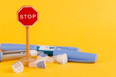 Glikoz kontrolü için bir semaglutit ilaç kaleminin yanına yerleştirilmiş tahta dur işareti, parlak sarı bir arka planda sergilenmektedir.