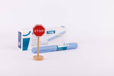 Diyabet kontrolü için bir semaglutit ilaç kaleminin yanına tahta dur tabelası konmuş, temiz beyaz bir arka planda fotoğraflanmış.