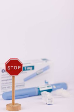 Şeker hastalığı ve glikoz yönetimi için kullanılan semaglutit içeren bir kalemin yanındaki tahta dur işareti beyaz arka planda görüntülenmiştir.