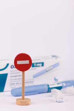 Diyabet yönetimi için Semaglutide kalemi, beyaz arka planda görünen küçük tahta dur işaretinin yanında.