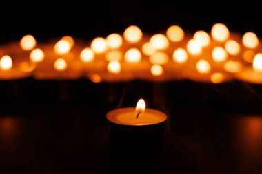 Parlak bir mum, duayı ve yansımayı simgeler. Siyah bir arkaplanda parlayan arka plan mumlarıyla.